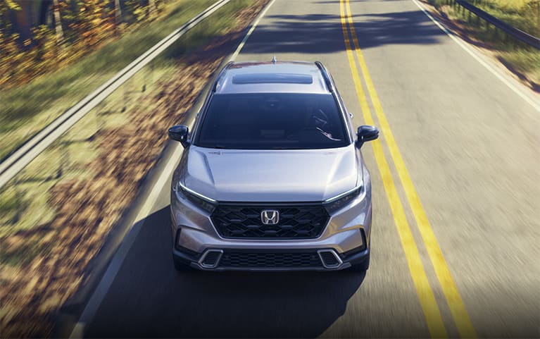 2027 Honda CR-V Sport Touring in Solar Silver Metallic top driving on a scenic winding forest road (Compact Crossover SUV).