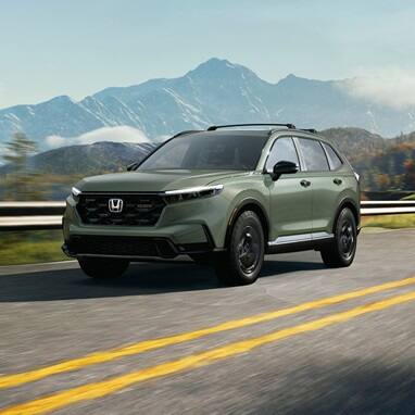 2027 Honda CR-V TrailSport Hybrid in Ash Green Metallic front driving on a scenic mountain road (Compact Crossover SUV).