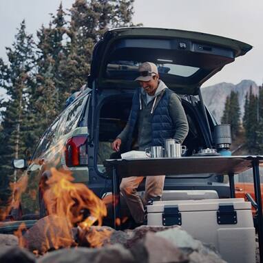 2027 Honda Passport TrailSport Elite in Ash Green Metallic back parked at a campsite with a campfire (Mid-Size SUV).