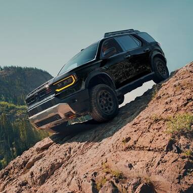 2027 Honda Passport TrailSport Elite in Crystal Black Pearl front driving up a steep rocky mountain slope (Mid-Size SUV).