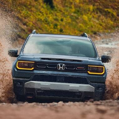 2027 Honda Passport TrailSport Elite in Smoke Blue Pearl front splashing through mud on an off-road trail (Mid-Size SUV).