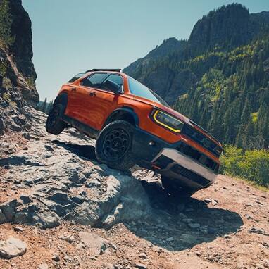 2027 Honda Passport TrailSport Elite in Sunset Orange front navigating a steep and rocky mountain trail (Mid-Size SUV).