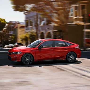 2027 Honda Civic Hatchback Sport Hybrid in Rallye Red profile driving on a city street (Compact Hatchback).